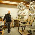 Ceel van Heijkop staat in zijn werkplaats met 2 zilverkleurige balonnen, 1 met cijfer 2 en een met 5