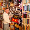 Rein van Willigen in zijn woonkamer met een afbeelding van het boek Mou$e entertainment en zilveren ballonnen op de achtergrond die het getal 25 vormen