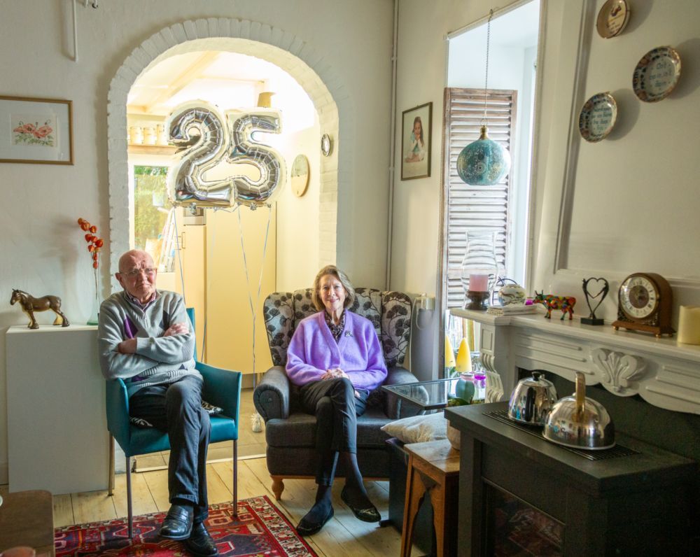 Nelly en Jaap Groot in hun huiskamer met een ballon op de achtergrond die het cijfer 25 vormt