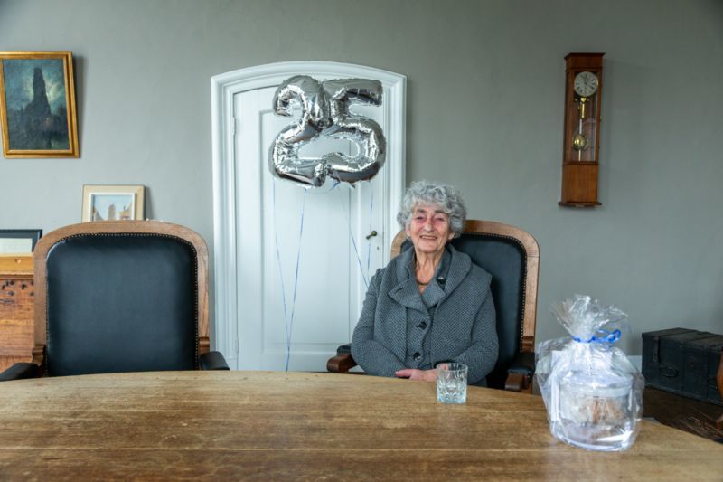 Nanny Peereboom in de oude burgemeesterskamer in het oude stadhuismet links in beeld zilveren ballonnen die het getal 25 vormen
