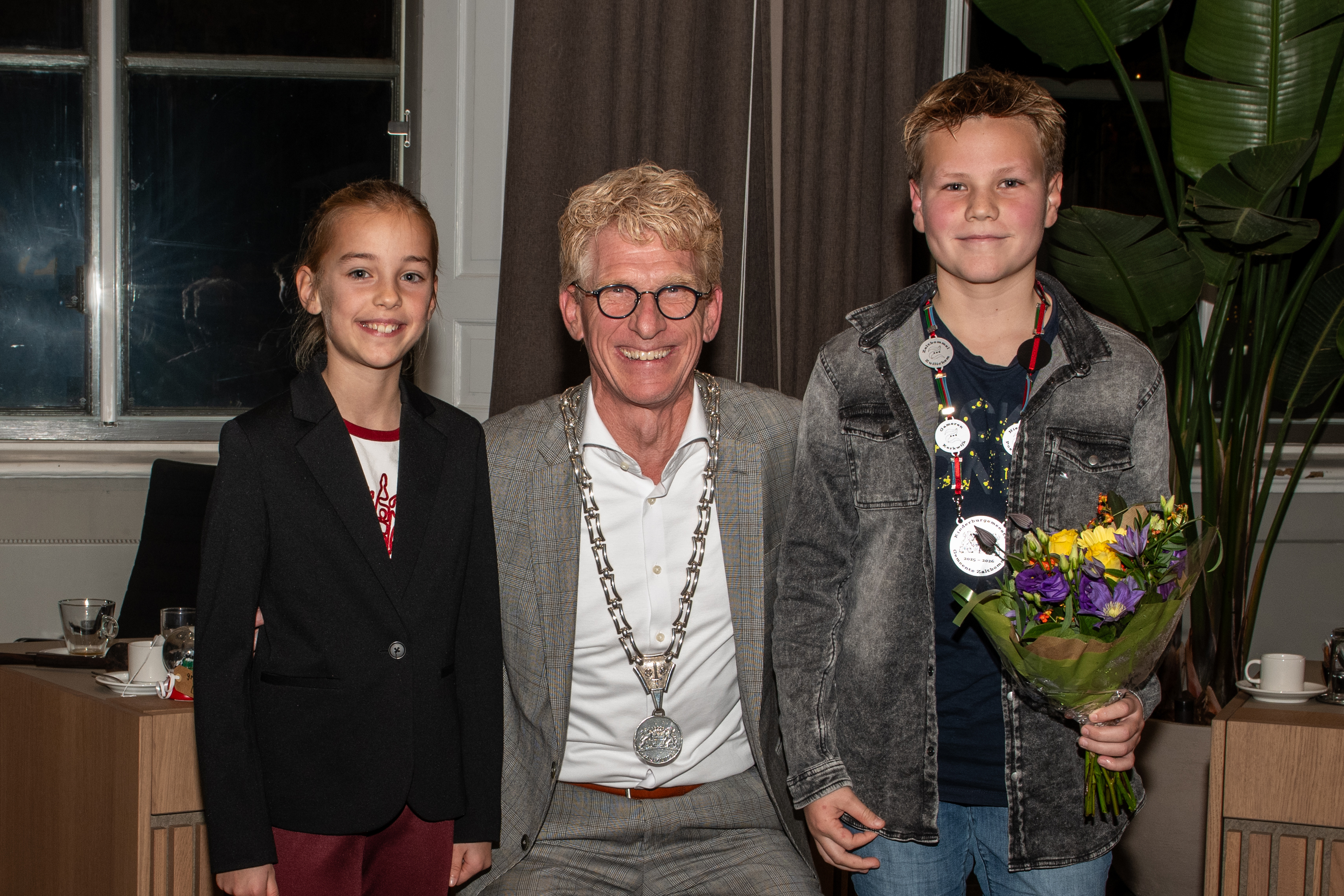 De burgemeester met ambtsketen en links van hem Liz en rechts Liam met de kinderambtsketen om en bosje bloemen in de hand
